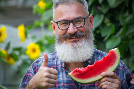 Portrait of mature bearded male farmer with red ripe watermelon, own harvest concept, selective focusの写真素材