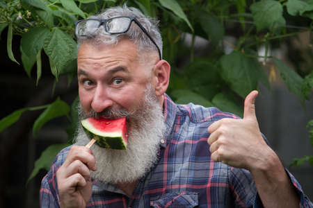 Portrait of mature bearded male farmer with red ripe watermelon, own harvest concept, selective focusの写真素材