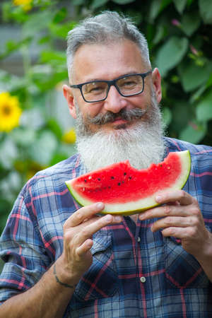 Portrait of mature bearded male farmer with red ripe watermelon, own harvest concept, selective focusの写真素材