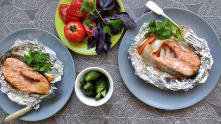 Top view two portions of homemade foil baked salmon steak and fresh vegetables, selective focusの写真素材