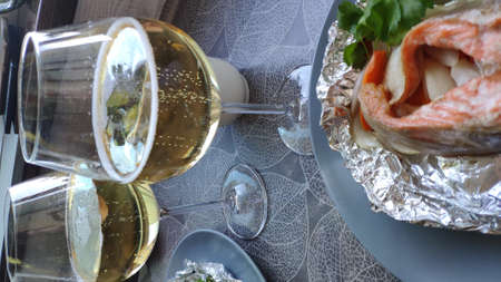 Top view two portions of foil baked salmon steak and two glasses of white wine, selective focusの写真素材