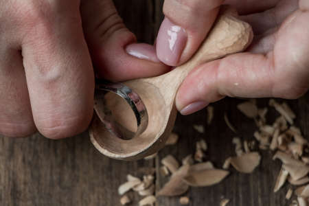 Handmade wooden utensils, top view female hands carve a wooden spoon with stock-knife, selective focusの写真素材
