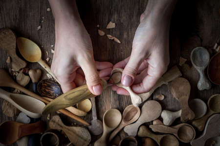 Handmade wooden utensils, top view female hands carve a wooden spoon with stock-knife, selective focusの写真素材