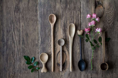 Top view few wooden spoons and rose branch on wooden table, eco friendly concept of cutlery, handmade tableware productionの写真素材