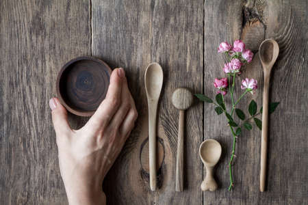 Top view few wooden spoons and rose branch on wooden table, eco friendly concept of cutlery, handmade tableware productionの写真素材
