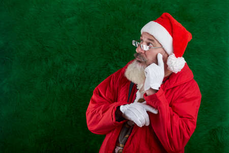 Mature bearded man with eyeglasses on face wearing Santa hat, Santa looks away at something, copy spaceの写真素材