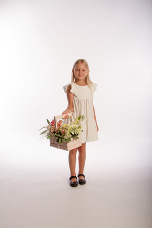 Studio portrait of cute blonde girl in white dress with wooden basket of flowers, white background, selective focusの写真素材