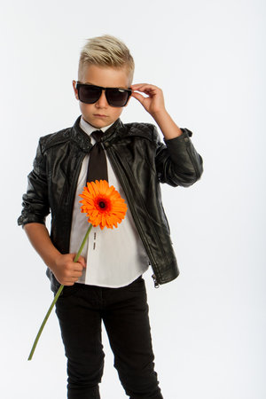 Studio portrait of fashionable blond caucasian boy with single gerbera flower, white background, copy spaceの写真素材