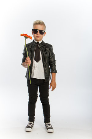 Studio portrait of fashionable blond caucasian boy with single gerbera flower, white backdrop, copy spaceの写真素材