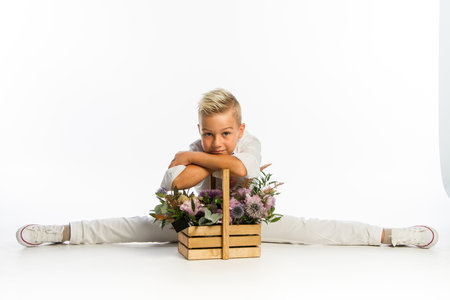 Studio portrait of fashionable blond caucasian boy with wooden basket of flowers, white backdrop, copy spaceの写真素材