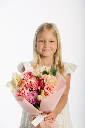 Studio portrait of cute blonde girl in white dress with wooden basket of flowers, white backdrop, selective focusの写真素材