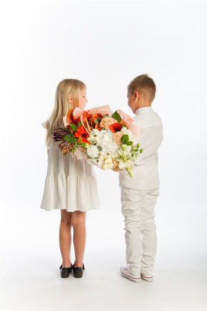 Studio portrait boy gives girl festive bouquet, congratulatory concept, white background, copy spaceの写真素材