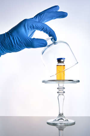 vaccine presentation concept, vial vaccine dose in glass cloche on mirror surface, white backdrop, selective focusの写真素材