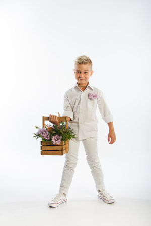Studio portrait of fashionable blond caucasian boy with wooden basket of flowers, white backdrop, copy spaceの写真素材