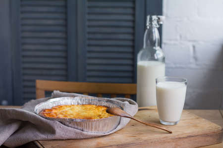 Cottage cheese casserole with cup and bottle of milk on wooden table background. Cottage cheese casserole.の写真素材