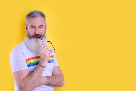 Confident mature bearded man dressed with  symbols t-shirt looking at camera, studio portrait of  man, yellow backgroundの写真素材