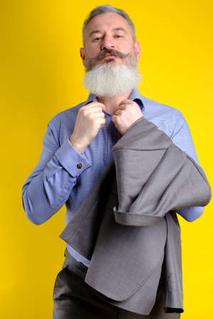 Studio portrait mature bearded handsome man in gray business suit looking to camera, work profession lifestyle, yellow background.の写真素材