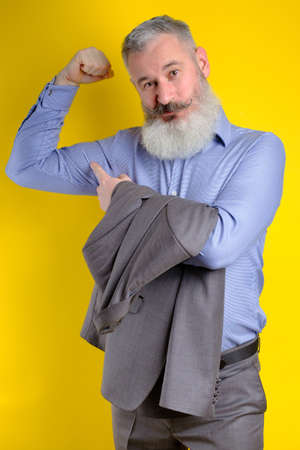 Studio portrait mature businessman dressed in grey suit shows his pumped up biceps, strong business, exercising in entrepreneurship concept.の写真素材