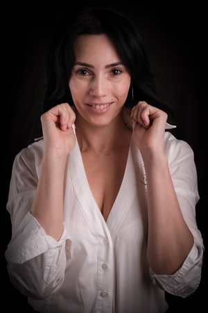 Portrait of beautiful mature brunette woman dressed in white shirt isolated on black backdrop, copy spaceの写真素材