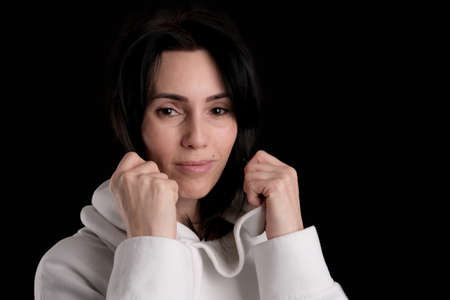 Portrait of beautiful mature brunette woman dressed in white hoodie isolated on black backdrop, copy spaceの写真素材
