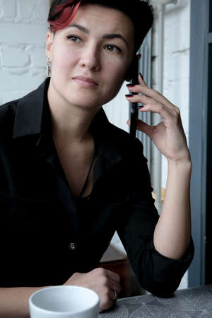 Portrait of attractive young adult woman talking on mobile phone with cup of hot beverageの写真素材