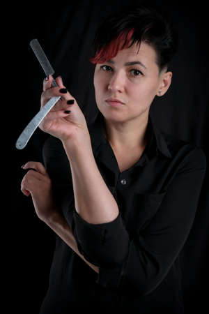 Half length portrait of young adult barber woman on black background holding vintage straight razor, modern barber girl conceptの写真素材