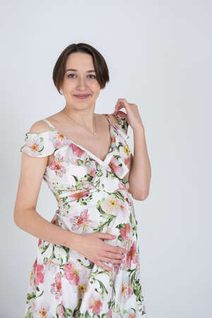 Studio portrait of cheerful young pregnant woman in summer dress on white grey background, happy pregnancy conceptの写真素材