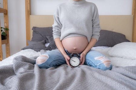 Pregnant woman with alarm clock on bed at home, giving birth soon conceptの写真素材