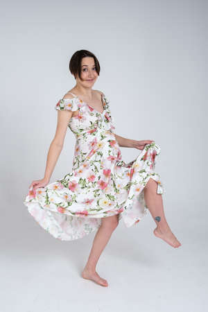 Studio portrait of cheerful young pregnant woman in summer dress on white gray background, happy pregnancy conceptの写真素材