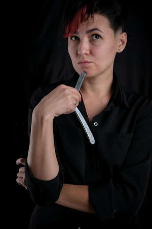 Half length portrait of young adult barber woman on black background holding vintage straight razor, modern barber girl conceptの写真素材