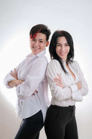 Portrait of two laughing women dressed in white clothes standing back to back isolated over white backgroundの写真素材