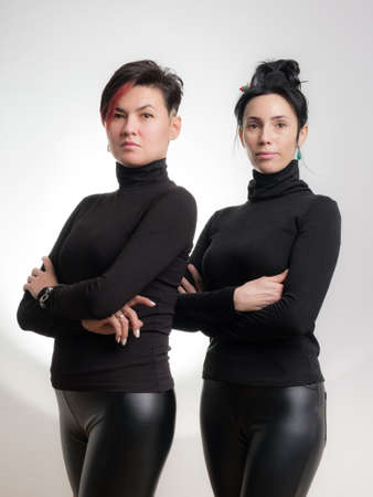 Portrait of two confident women dressed in black clothes standing side by side isolated over white backgroundの写真素材