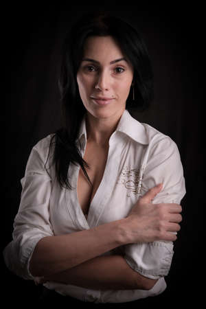 Portrait of beautiful mature brunette woman dressed in white shirt isolated on black backdrop, copy spaceの写真素材