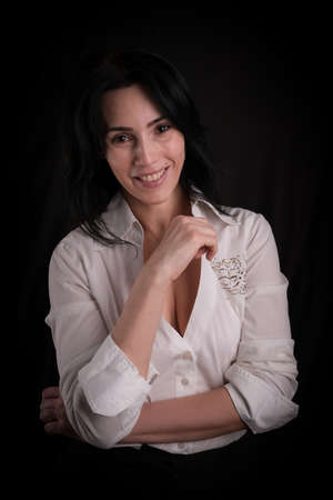 Portrait of beautiful mature brunette woman dressed in white shirt isolated on black backdrop, copy spaceの写真素材