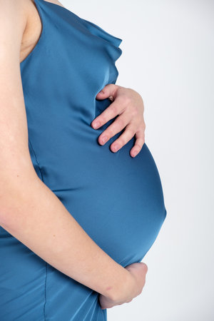 Studio portrait of young adult pregnant woman in blue dress on white grey background, happy pregnancy conceptの写真素材