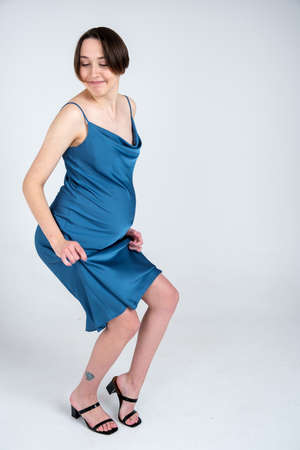 Studio portrait of young adult pregnant woman in blue dress dancing on white grey background, happy pregnancy conceptの写真素材