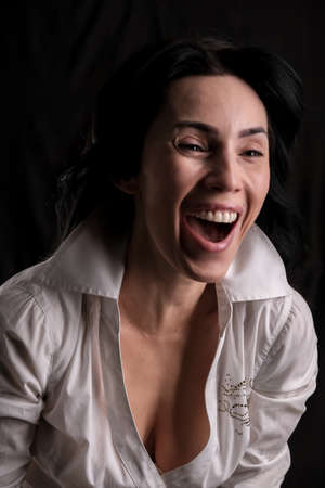 Portrait of beautiful mature brunette woman dressed in white shirt isolated on black backdrop, copy spaceの写真素材
