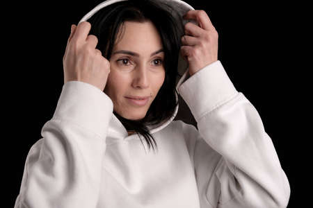 Portrait of beautiful mature brunette woman dressed in white hoodie isolated on black backdrop, copy spaceの写真素材