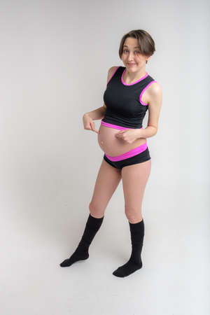 Young adult pregnant girl in sportswear. Sport and pregnancy concept. Yoga and fitness in anticipation of childbirth. White backdrop.の写真素材