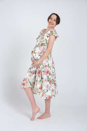 Studio portrait of cheerful young pregnant woman in summer dress on white grey background, happy pregnancy conceptの写真素材