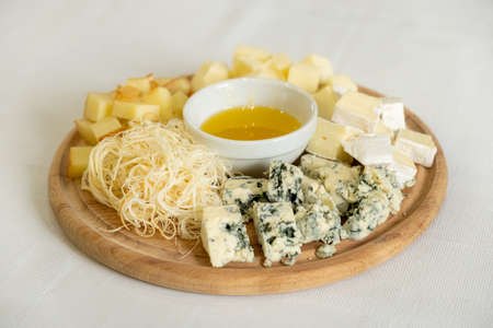 Wooden board with various types of cheeses and bowl of honey, healthy snack, selective focusの写真素材