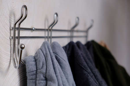 Extremely close-up various clothes hang on metal wall hanger, hooks with clothes hangers on white wall, selective focusの写真素材