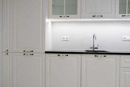 Modern and elegant kitchen with white drawers and cupboards, black marble countertop and built in sink with silver tapの写真素材