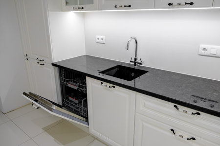 Side view modern and elegant kitchen with white drawers and cupboards, black marble countertop and built in sink with silver tapの写真素材