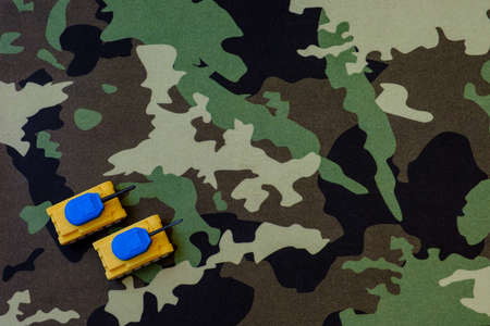 Yellow-blue tanks figures on camouflage background, Ukrainian flag colors on toy tank figures, anti-war concept, selective focusの写真素材
