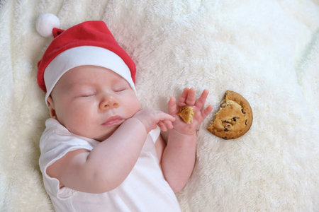 A two-month-old baby dressed in a festive Christmas outfit, lying with milk and cookies on a bright background, radiating holiday cheer and coziness.の写真素材