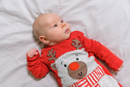 An adorable baby boy in a festive Christmas outfit sitting peacefully on a bright, light-colored background. A heartwarming and cheerful holiday scene.の写真素材