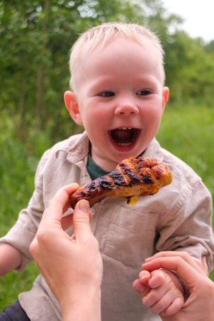 Happy toddler excited about grilled chicken at picnic