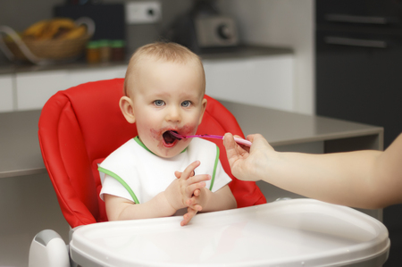 A small child eats jam and cereal, sits on a highchairの写真素材