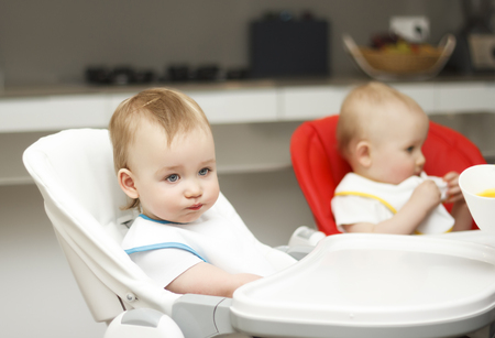 Happy toddler sitting in highchair and eating porridge. Baby learning to eat and has yogurt on porridge.の写真素材